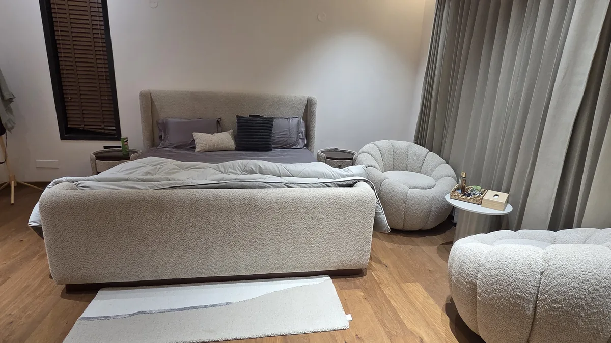 Custom king-size bed with cream bouclé upholstered headboard and footboard storage, bouclé swivel chair and ottoman — Flamingo Lifestyles bedroom