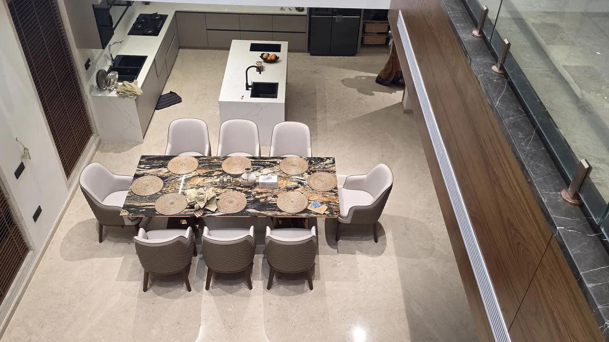 Overhead view of a custom marble-top 8-seater dining table in an open-plan Bengaluru villa with island kitchen behind — Flamingo Lifestyles space-planning example