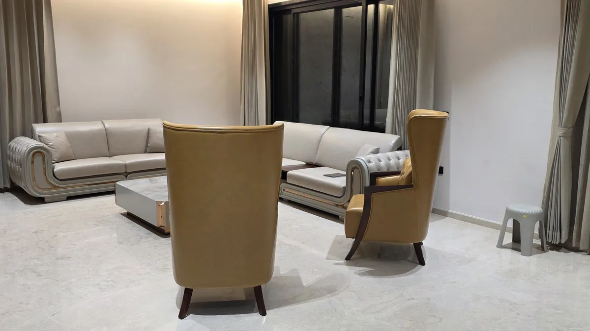 Curved cream Chesterfield-style custom sofa with tan leather wingback accent chairs in a Bengaluru villa living room — Flamingo Lifestyles bench-made furniture